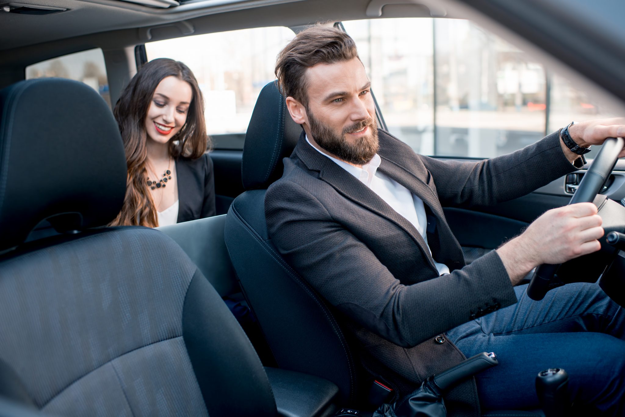 Beautiful businesswoman sitting on the backseat with elegant man driving the car in the city